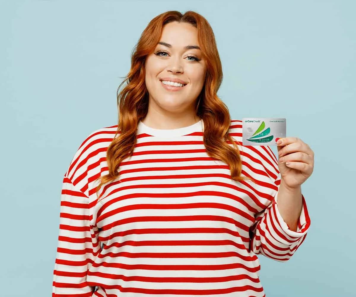 Smiling woman in a striped shirt holding a CareCredit card
