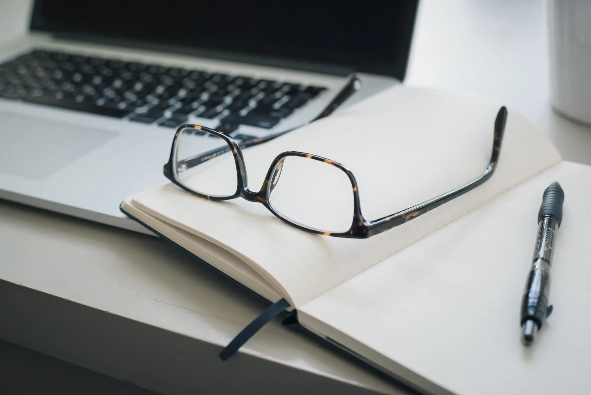 Laptop, reading glasses, and a notebook on a desk